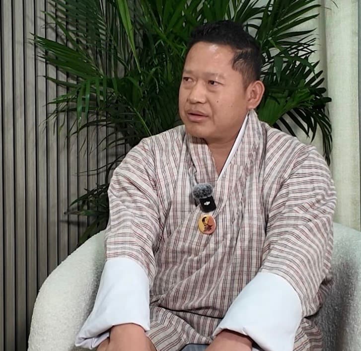 Kencho Tempa in a light-coloured gho during a calm BWK studio portrait.