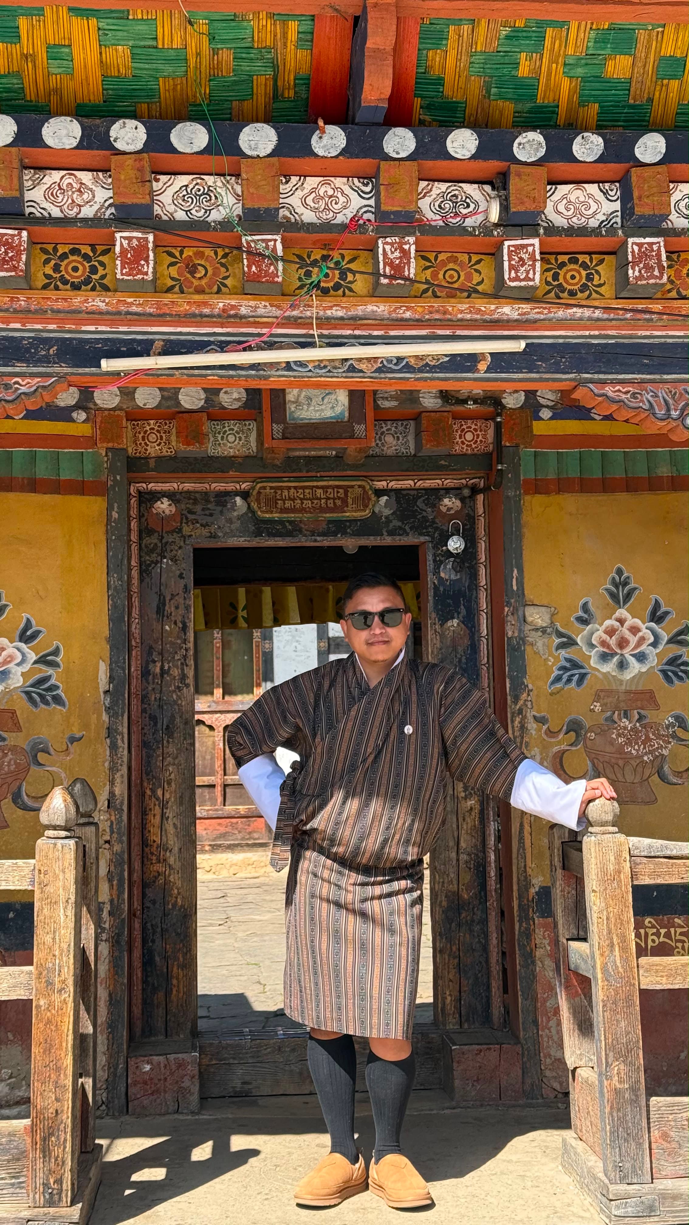 Thinley Dorji standing in traditional dress with camera equipment, representing BWK production support.